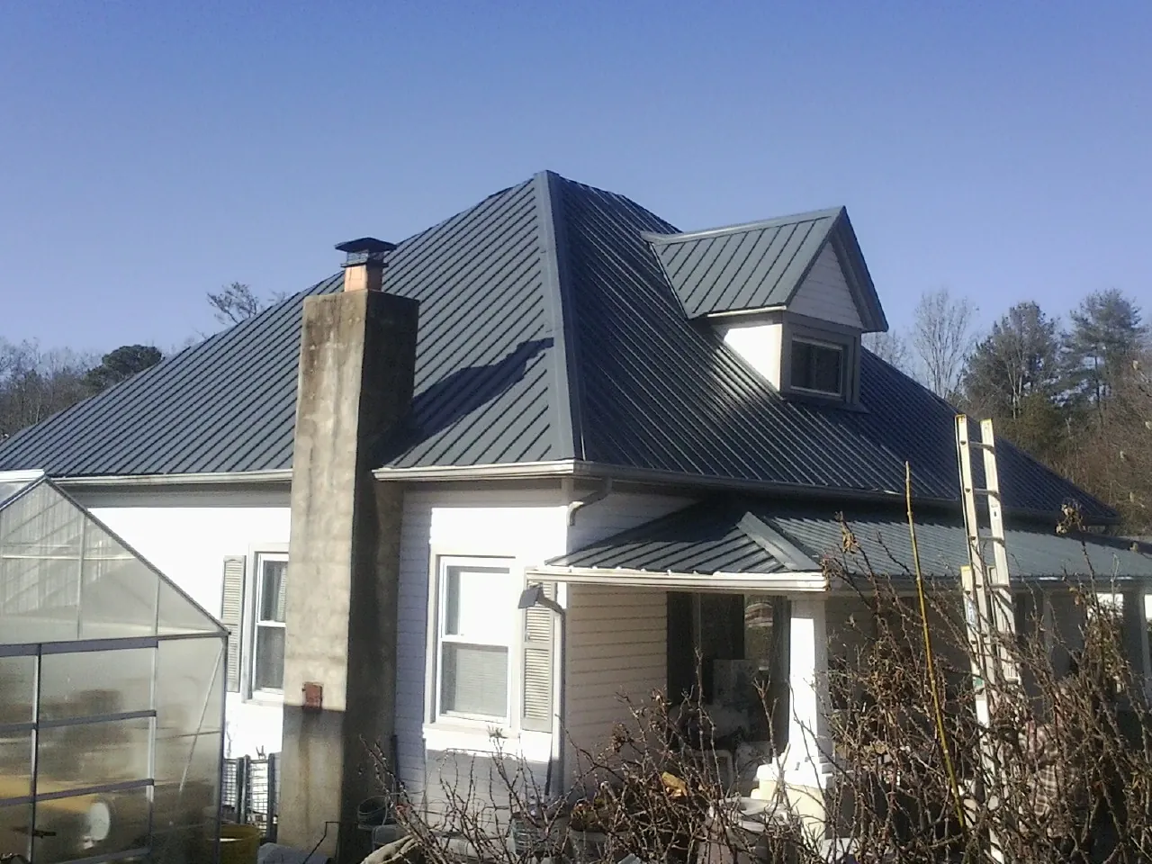 Dark blue standing seam metal roof on a white farmhouse with dormer — Slate & Tile Roof Repair by Roofing Brothers in Eagle Springs
