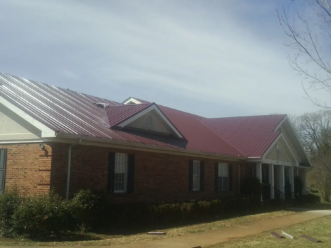 Red metal roof with gabled entries on a long brick building, from a Hail Damage Roof Repair job in Eagle Springs