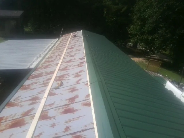 Old rusted panels beside newly installed green metal roofing — Wind Damage Roof Repair by Roofing Brothers in Eagle Springs