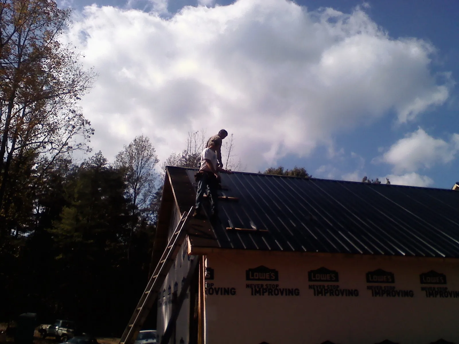 Roofer fastening dark metal panels high against a cloudy sky, from a Roof Inspection job in Eagle Springs