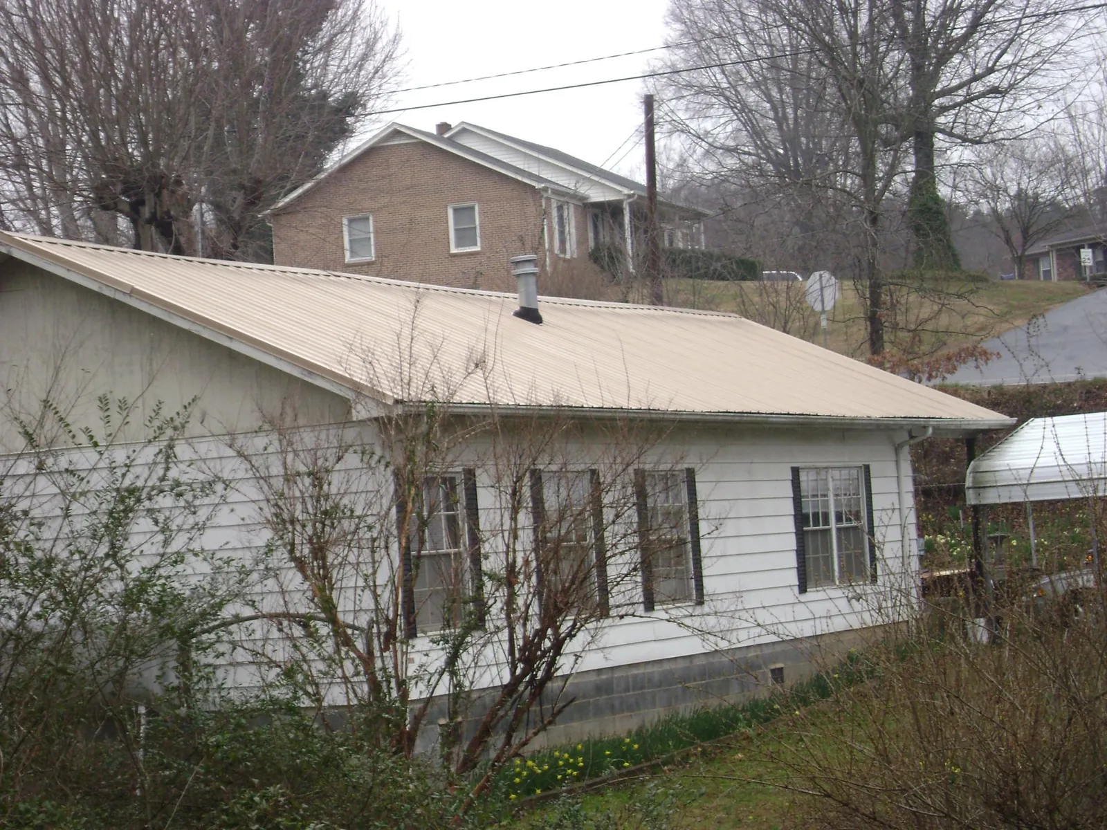 Tan metal roof on a white sided house set into a hillside — Commercial Roofing by Roofing Brothers in Eagle Springs