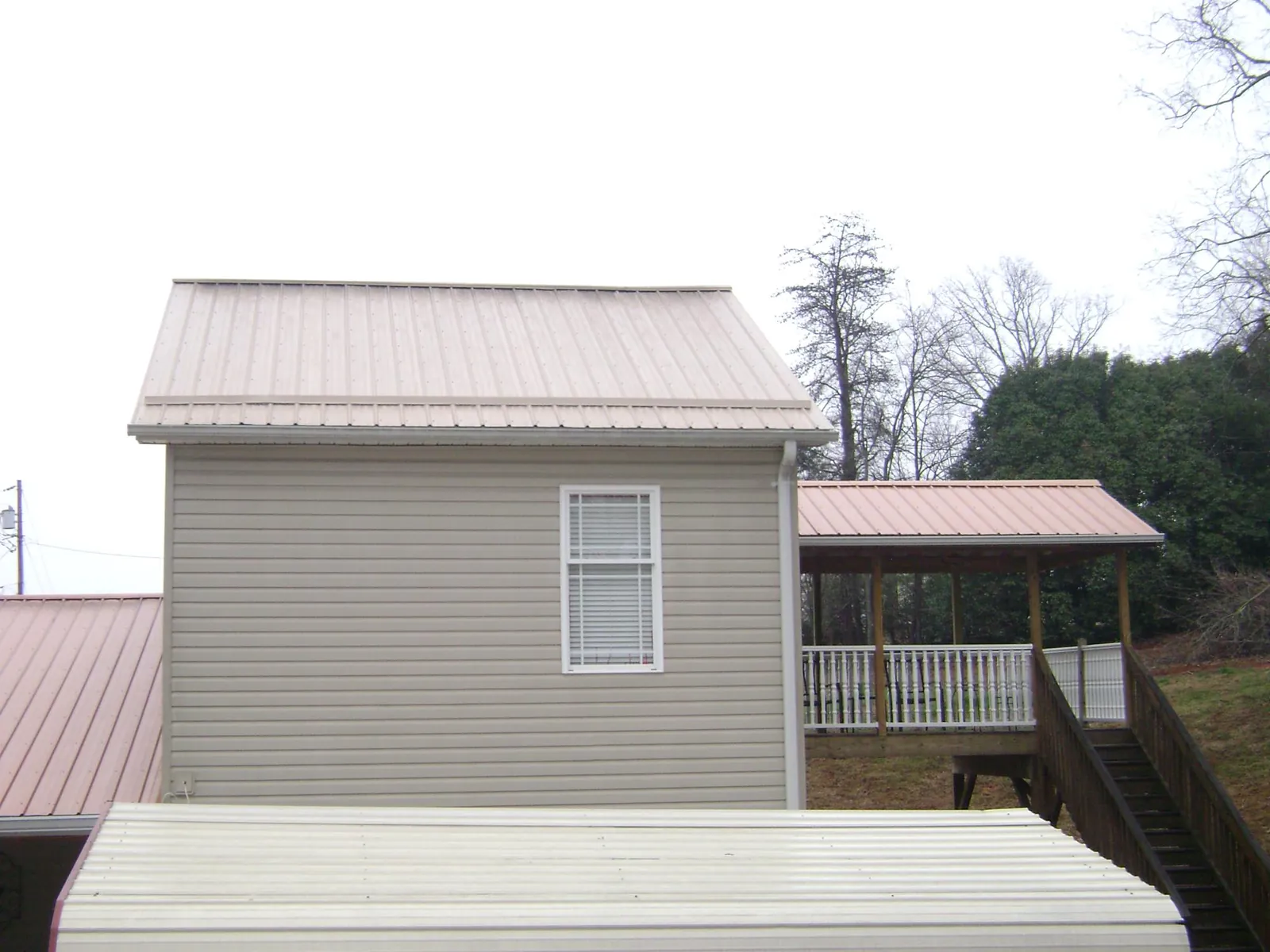 Tan metal roofs on a two story addition and attached porch, from a Roof Replacement job in Eagle Springs